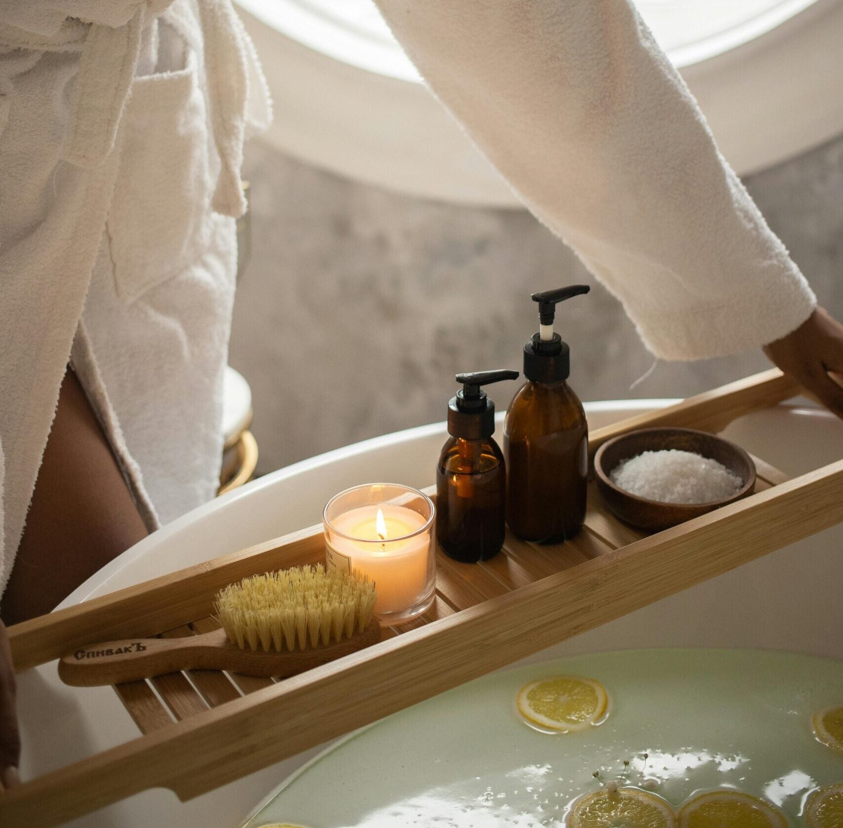 Person in a bathrobe setting up a bath with misc bathing items