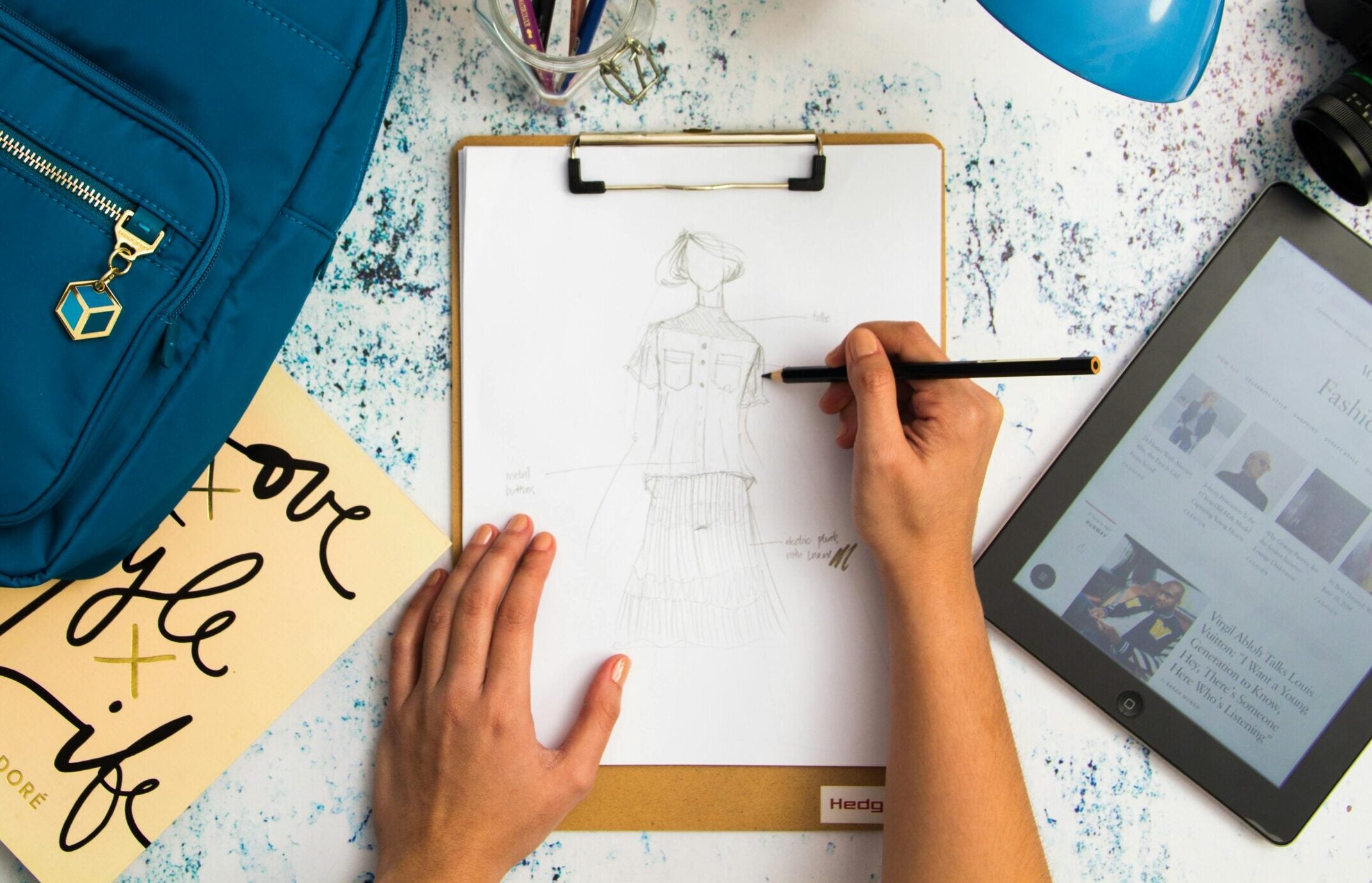fashion designer's desk with drafts, tablet, and backpack
